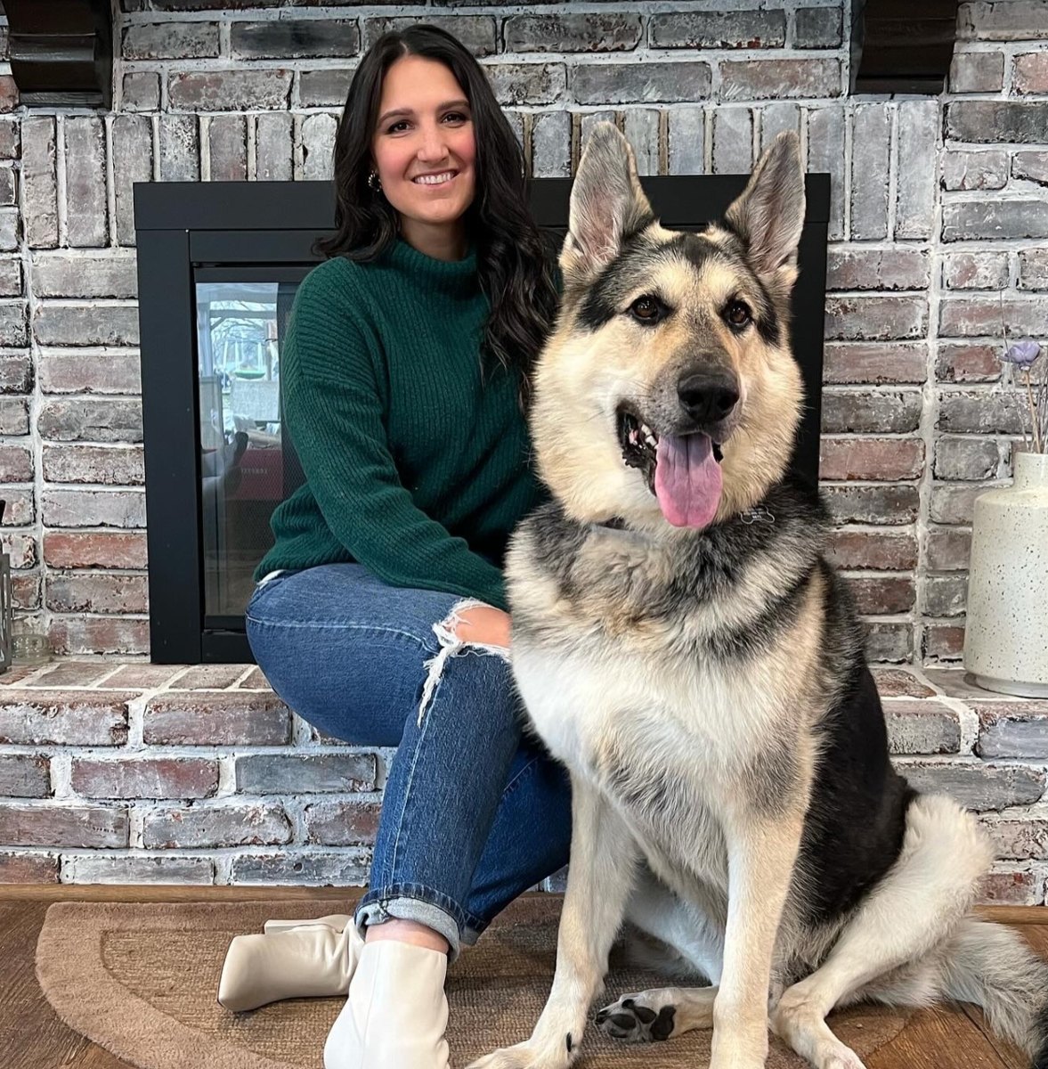 Meg sitting by a brick fireplace next to her German Shepherd